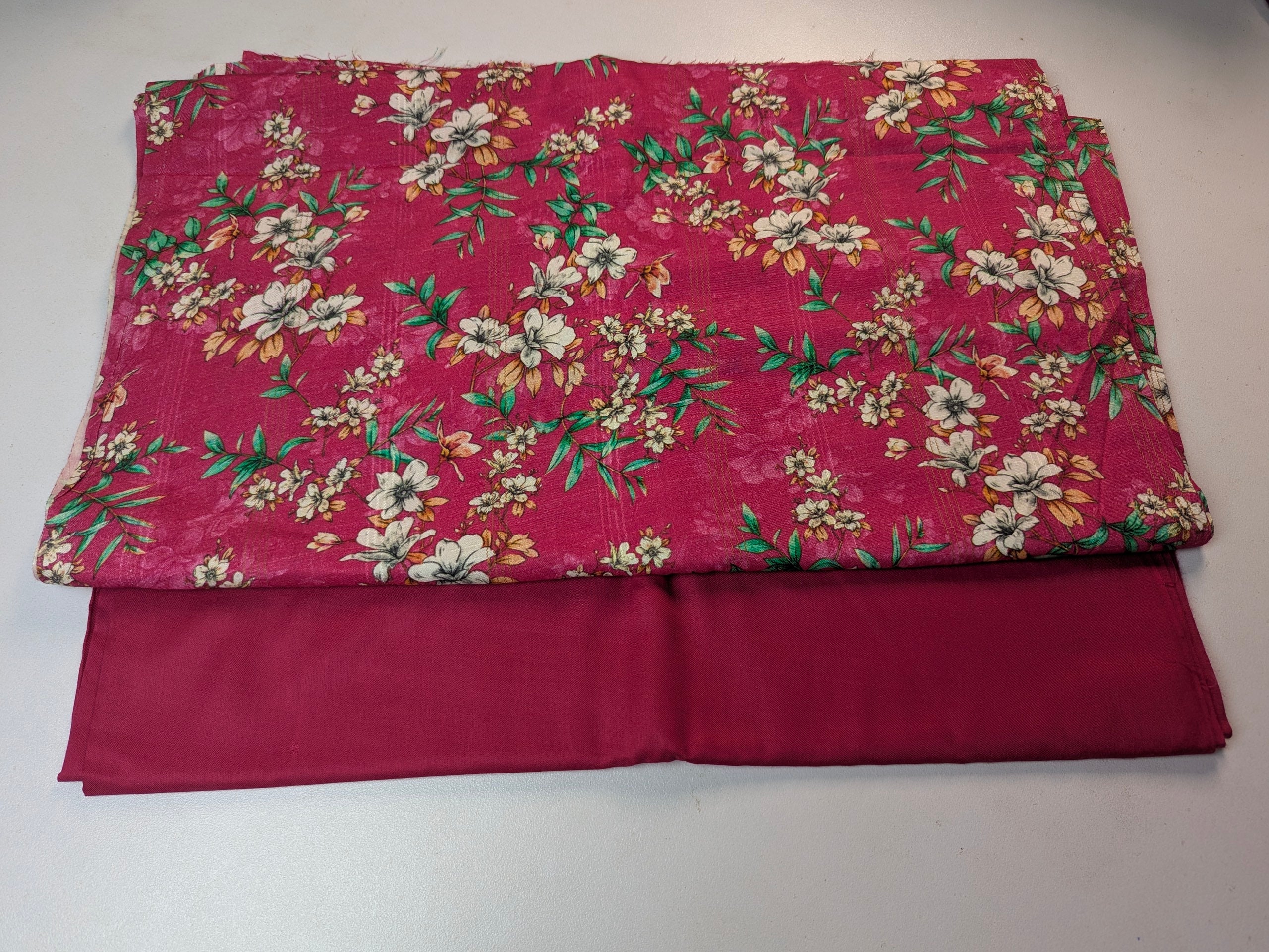 Two pieces of fabric, one plain and one with floral pattern, on a white background.